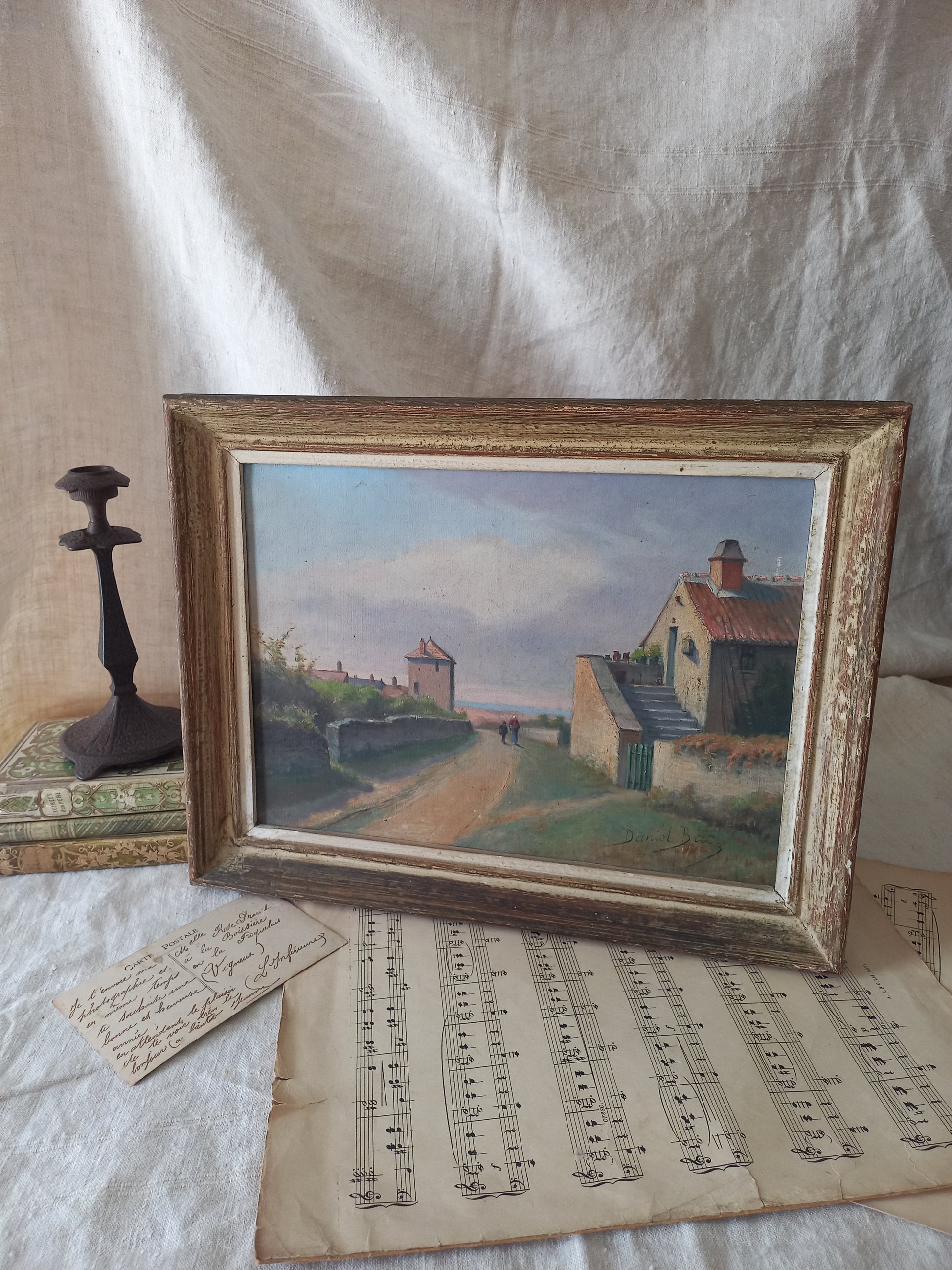 Framed painting of a rural, coastal village scene with sheet music underneath