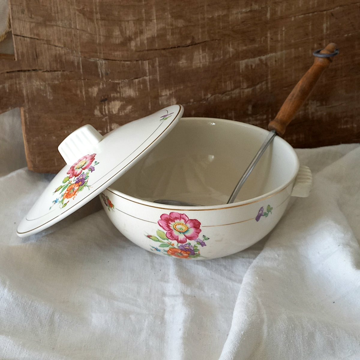 Decorative ceramic bowl with floral lid and floral pattern on a white cloth against a wooden background