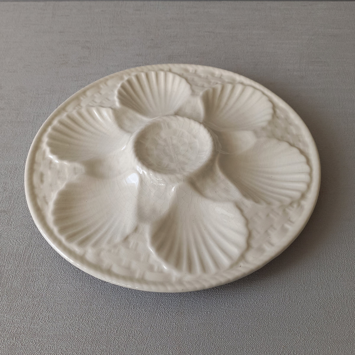 A beautiful French vintage oyster plate by Chantilly in a lovely shade of creamy white. This plate is a heavy, quality piece with six scalloped hollows for your oysters and a central hollow for a piece of lemon. There is a basket weave pattern and also a twisted rope pattern with some wonderful crazing in the glaze of this superb majolica plate which make it an eye catching piece of decor.