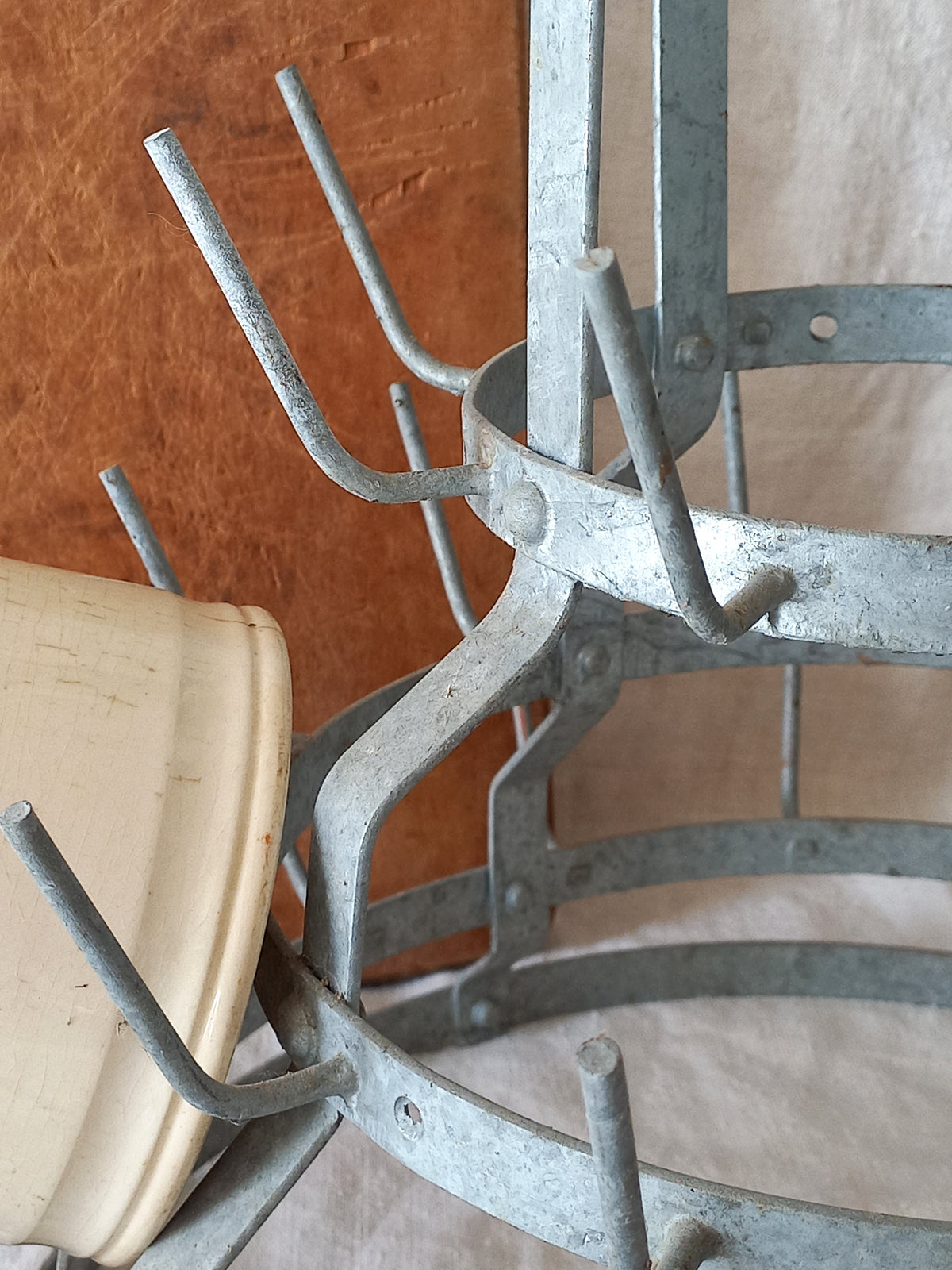 Galvanized metal plant hanger rack with multiple curved hooks, shown holding a beige plastic pot against a brown and beige background.