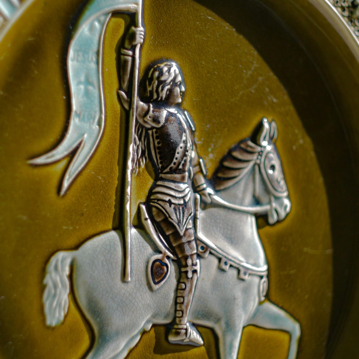 A large vintage/antique majolica wall plate with hand-coloured details in relief, the theme of the plate being the Patron Saint of France - Joan of Arc riding into battle with her banner (in French she is called Jeanne D'Arc).

This wonderful French decorative plate has a rich gloss finish, the glaze even being applied to the underside.

Around the lightly scalloped circumference of this large plate are patriotic symbols such as 'En Avant' (Go Forward), 'Honneur' (Honour) and 'Patrie' (Homeland).