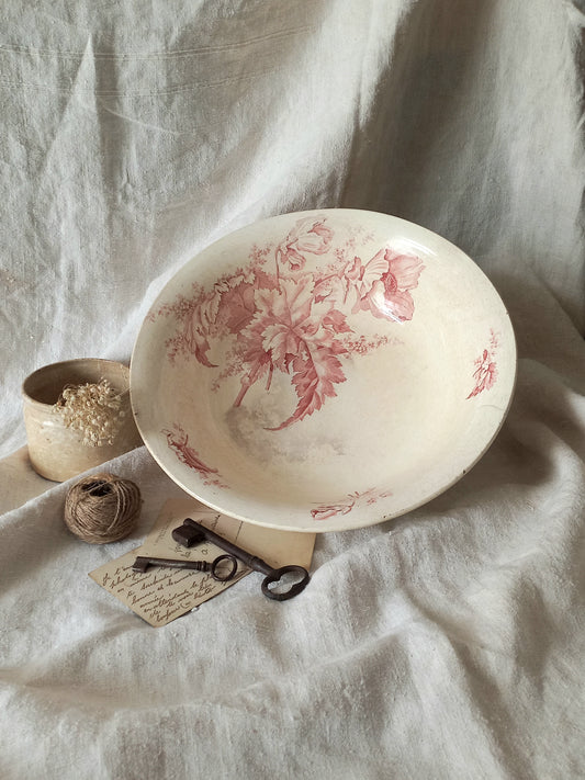 A large French ironstone bowl with deep pink floral pattern on a creamy white base. This antique piece has aged naturally over time, showing fine crazing, tea-staining, and small imperfections that reflect its long history.