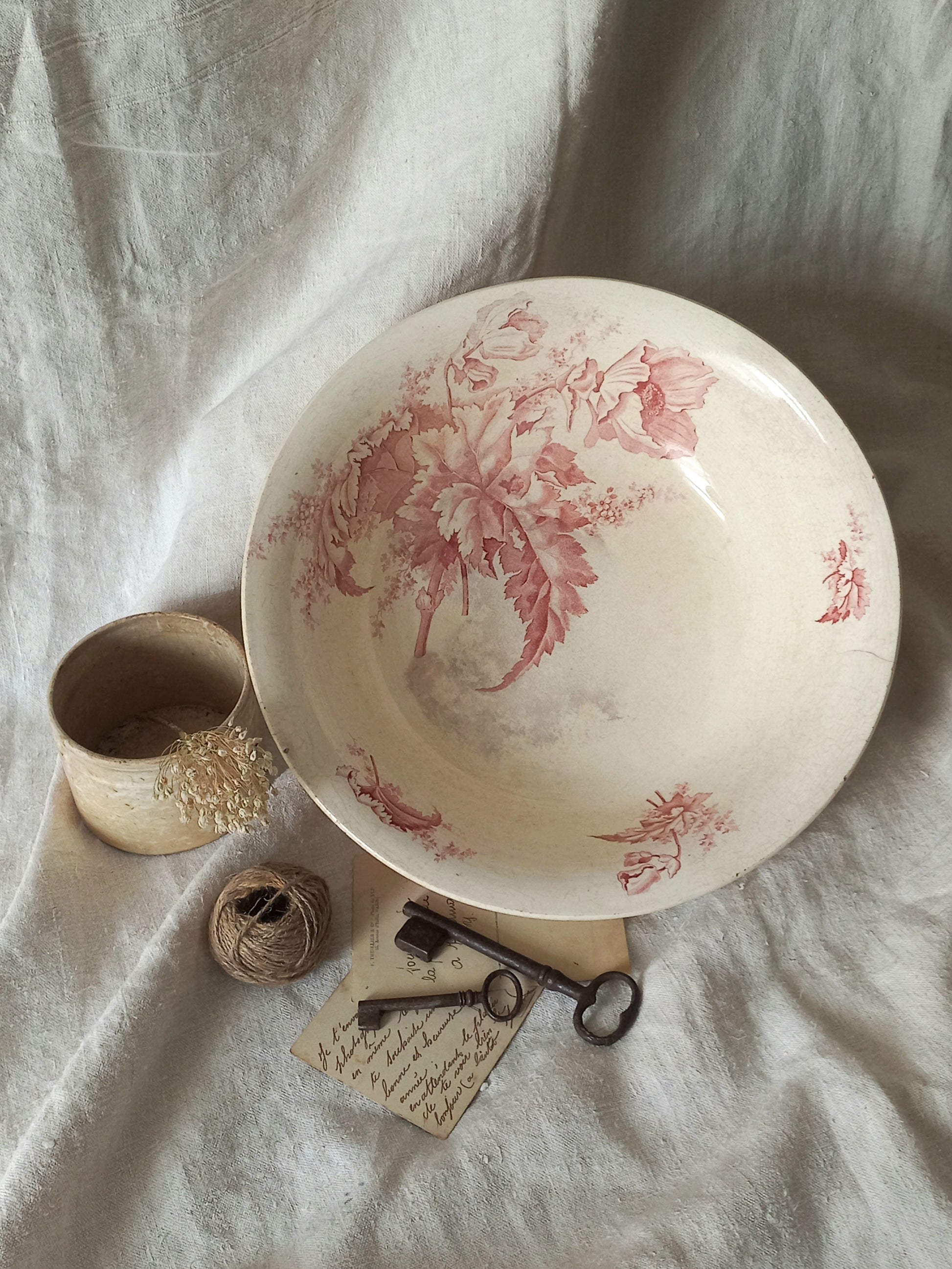 A large French ironstone bowl with deep pink floral pattern on a creamy white base. This antique piece has aged naturally over time, showing fine crazing, tea-staining, and small imperfections that reflect its long history.