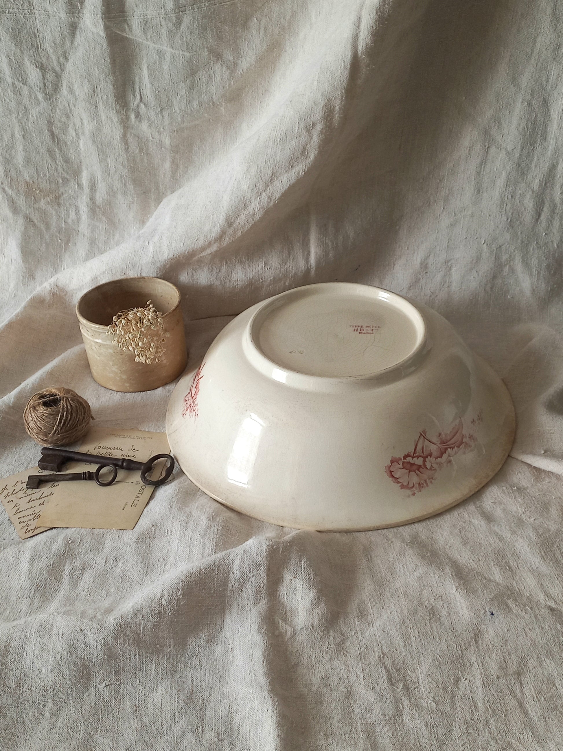 A large French ironstone bowl with deep pink floral pattern on a creamy white base. This antique piece has aged naturally over time, showing fine crazing, tea-staining, and small imperfections that reflect its long history.