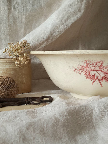 A large French ironstone bowl with deep pink floral pattern on a creamy white base. This antique piece has aged naturally over time, showing fine crazing, tea-staining, and small imperfections that reflect its long history.