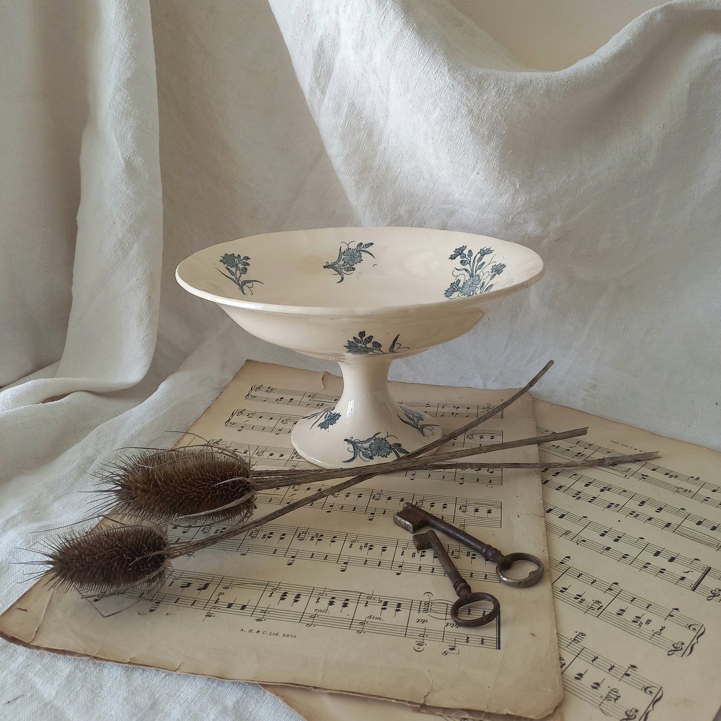 A beautiful antique compote or footed bowl by French manufacturer Longchamp. The main colour is a warm cream/white with blue floral transferware pattern.
