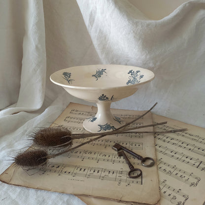 A beautiful antique compote or footed bowl by French manufacturer Longchamp. The main colour is a warm cream/white with blue floral transferware pattern.