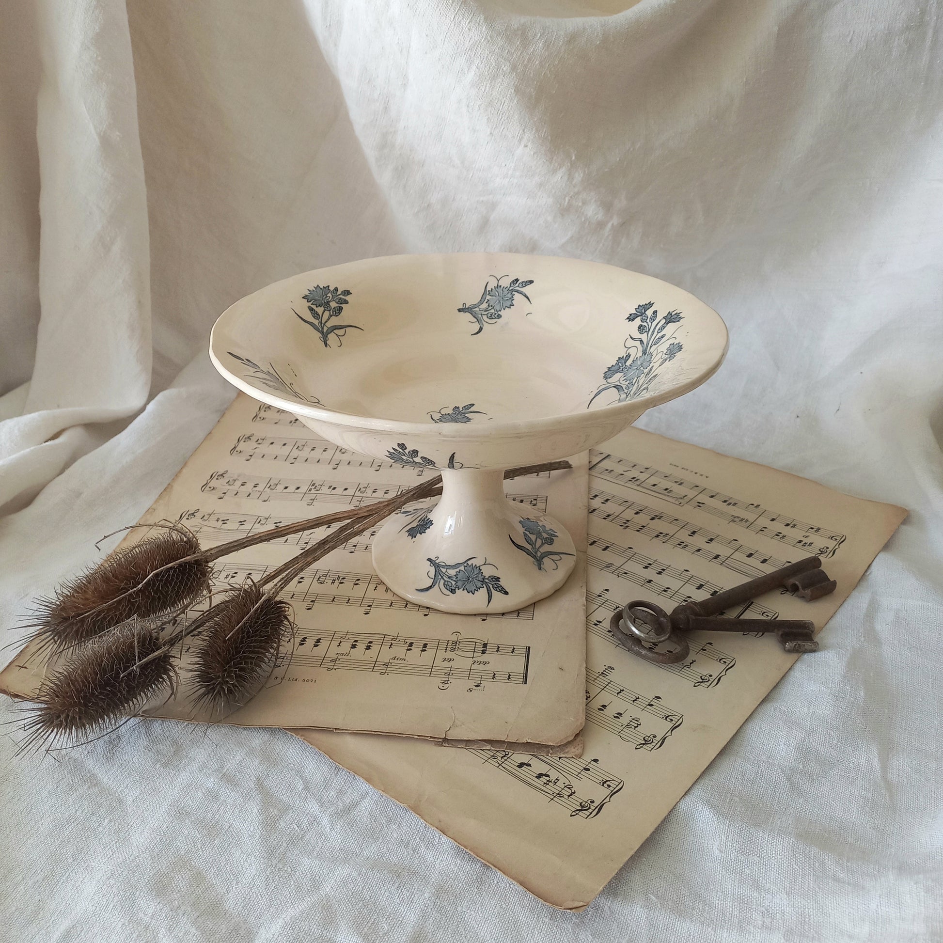 A beautiful antique compote or footed bowl by French manufacturer Longchamp. The main colour is a warm cream/white with blue floral transferware pattern.