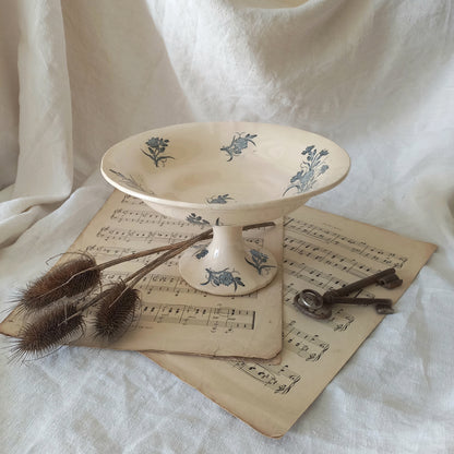 A beautiful antique compote or footed bowl by French manufacturer Longchamp. The main colour is a warm cream/white with blue floral transferware pattern.