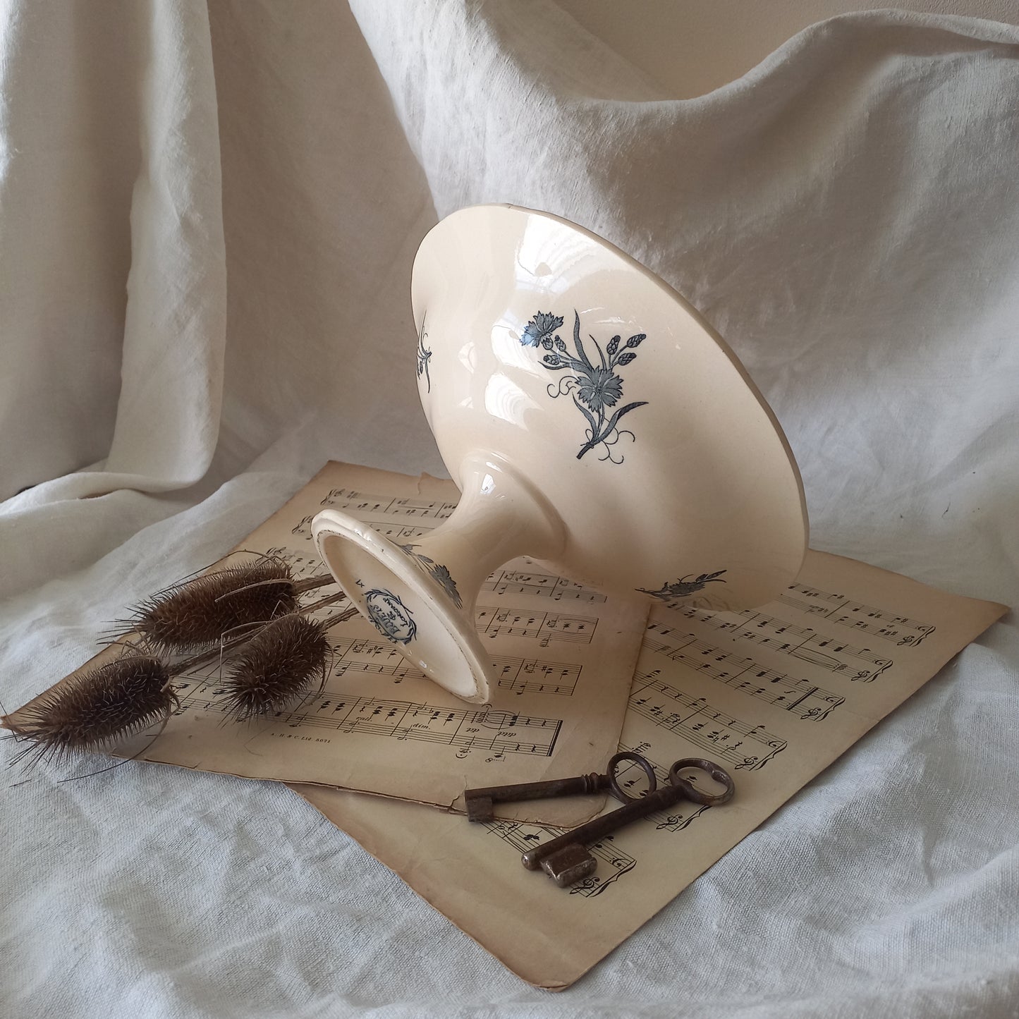 A beautiful antique compote or footed bowl by French manufacturer Longchamp. The main colour is a warm cream/white with blue floral transferware pattern.