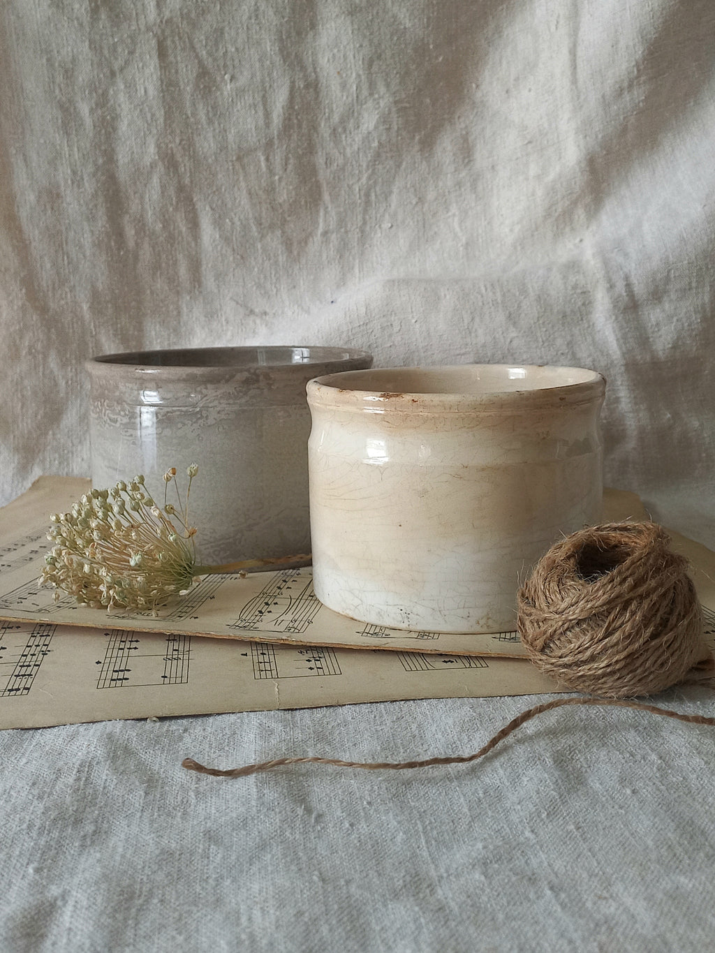 Two ceramic pots and a ball of twine on a textured surface with sheet music underneath.