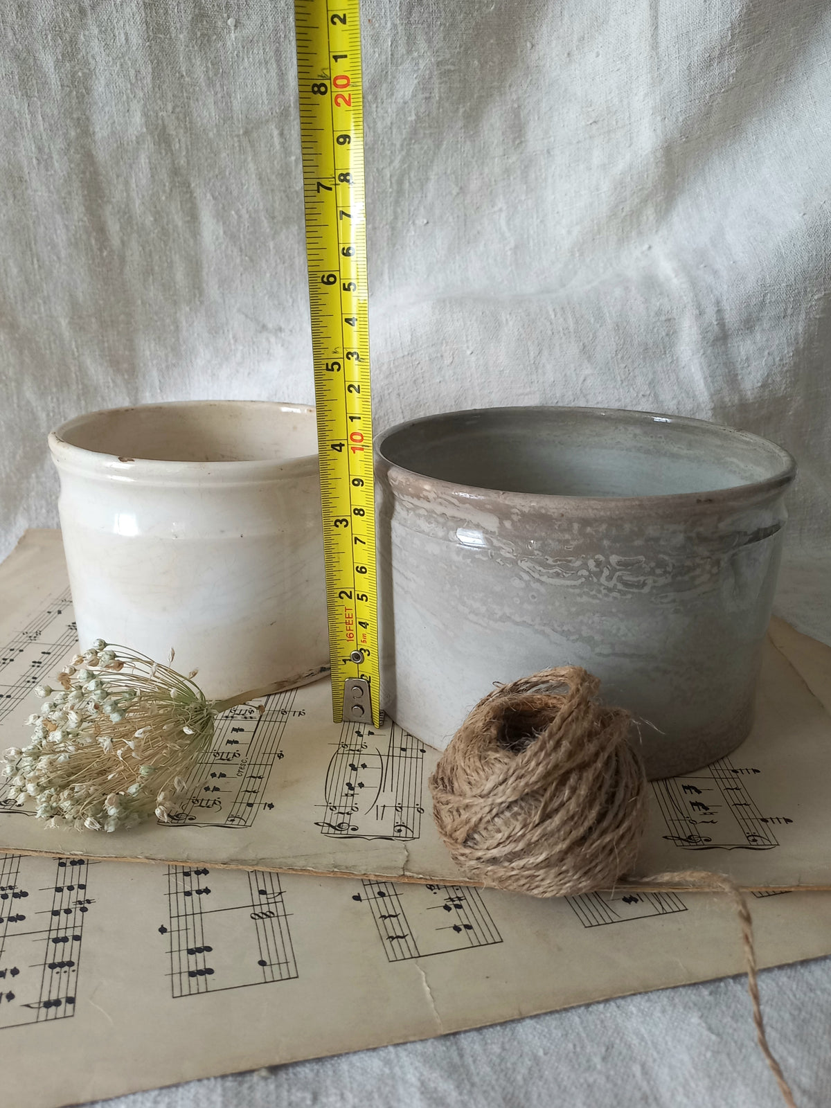 Two ceramic pots with a measuring tape, twine, and dried flowers on sheet music.