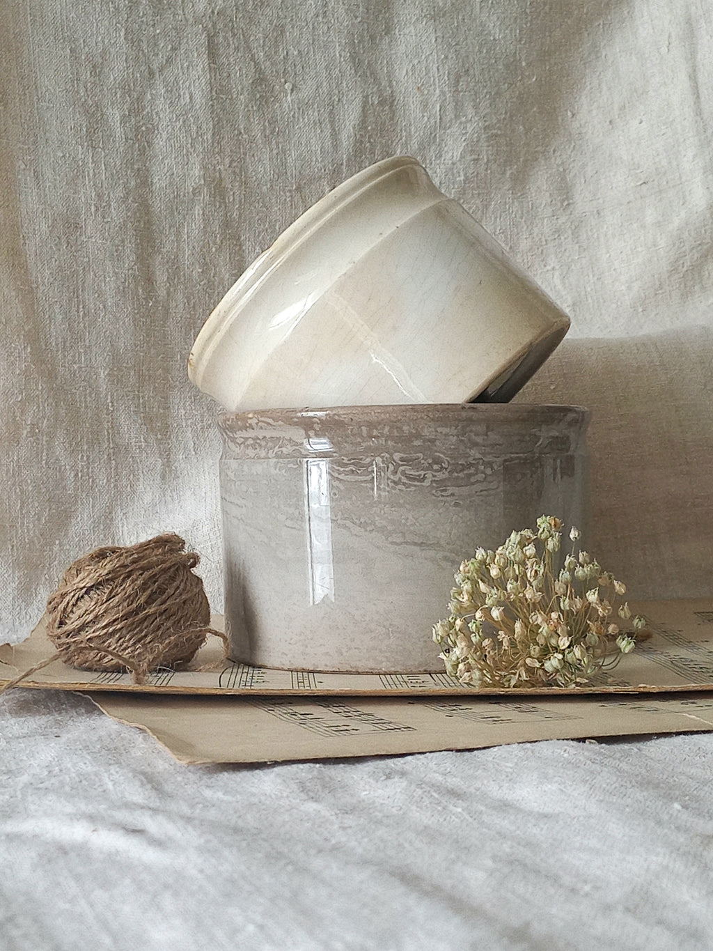 Two ceramic pots on a textured surface with dried flowers and twine.