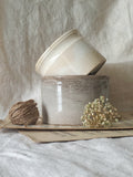 Two ceramic pots on a textured surface with dried flowers and twine.