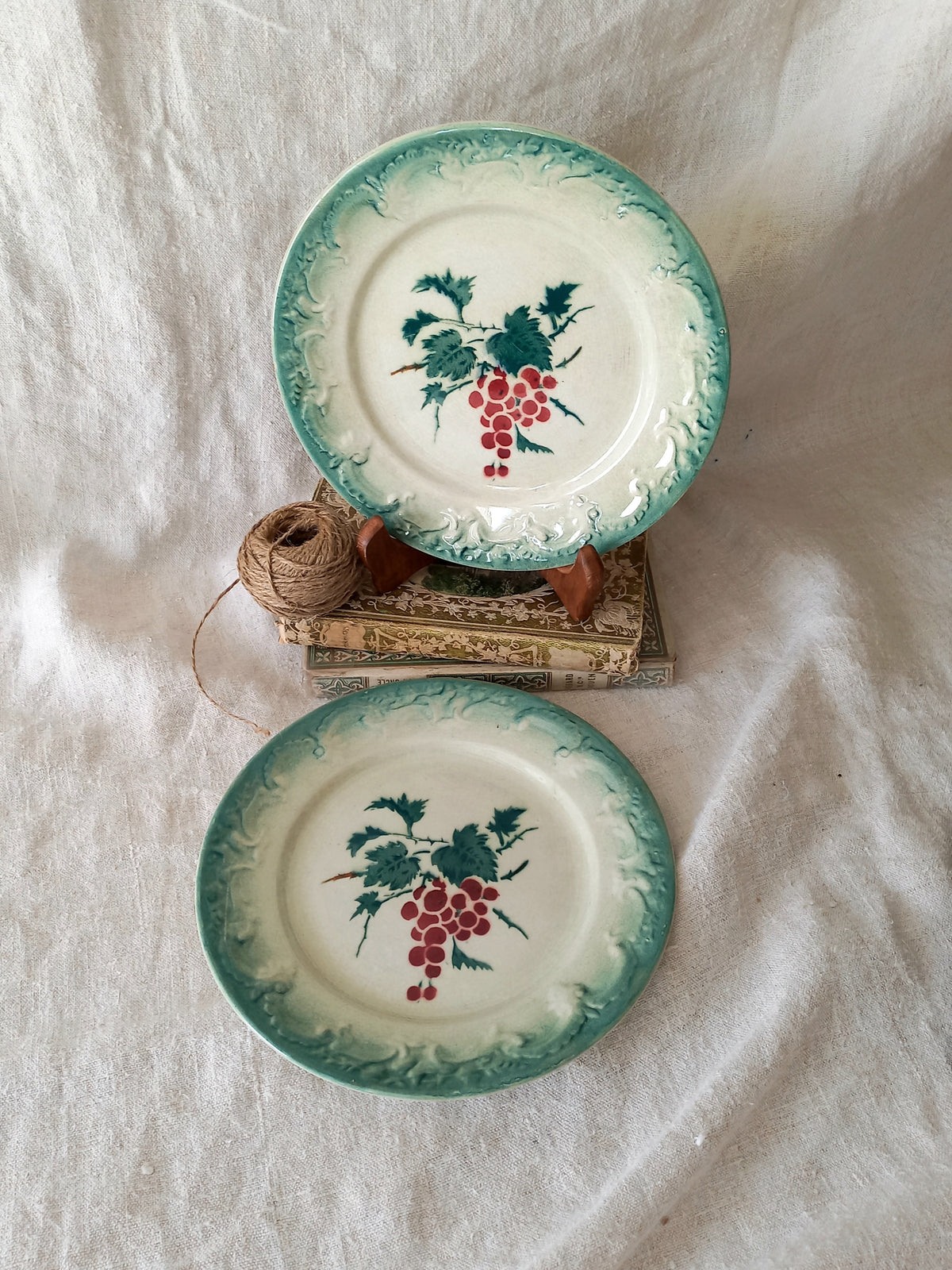 Two ceramic plates with grape design on a textured white surface