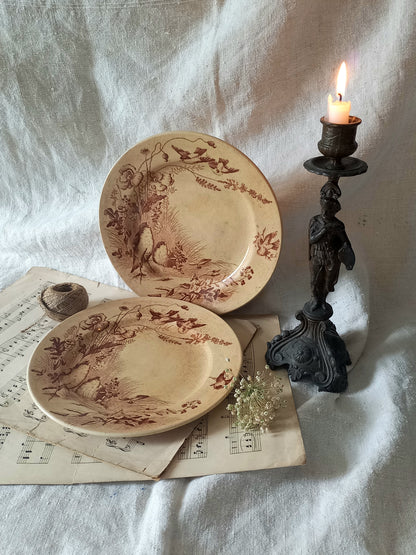 Two decorative antique plates with intricate designs on a white fabric background with a candle.