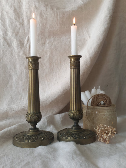 Two brass candlesticks with lit candles on a textured white surface.