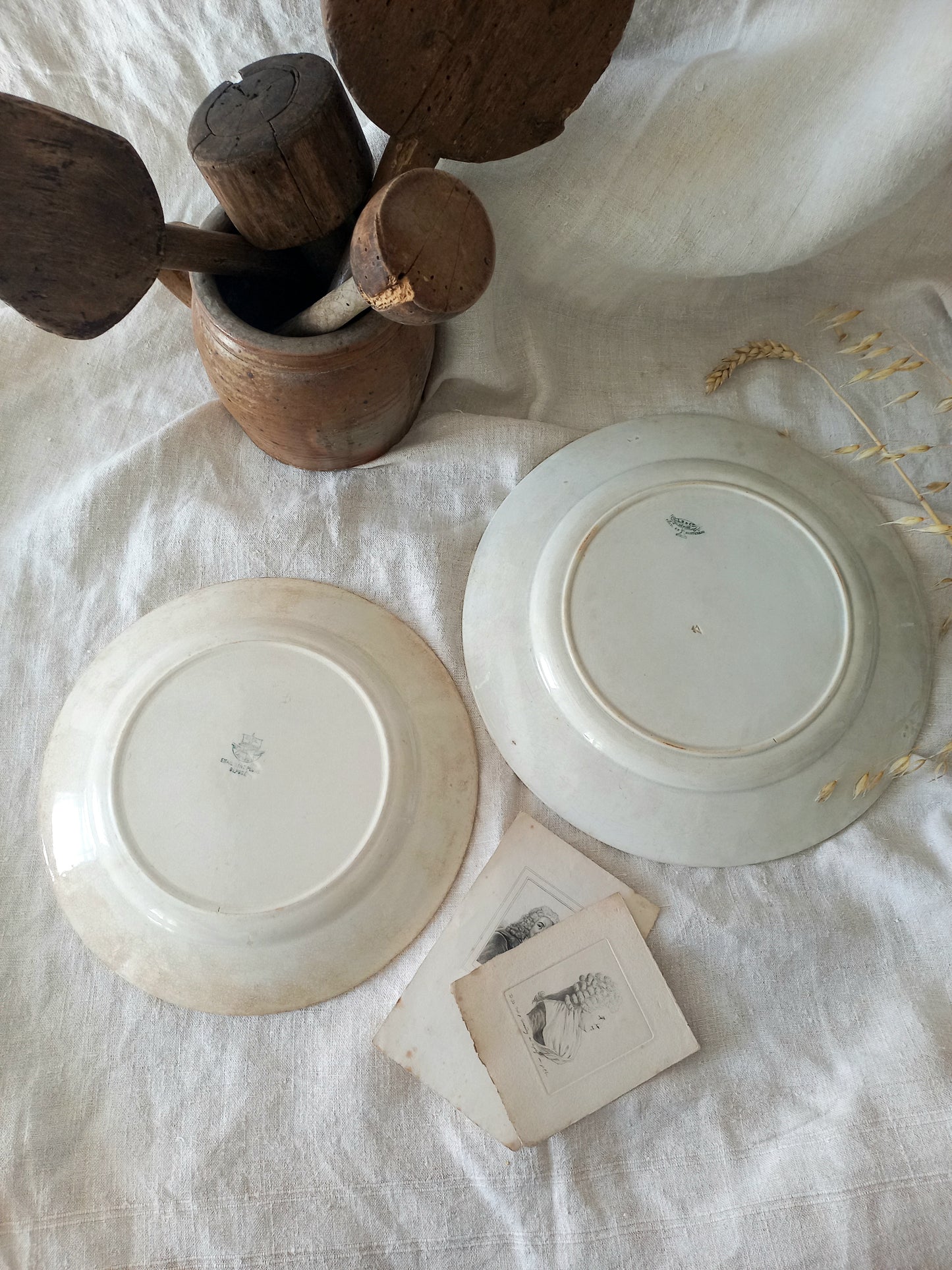 Two antique plates on a textured surface with wooden spoons and cards.
