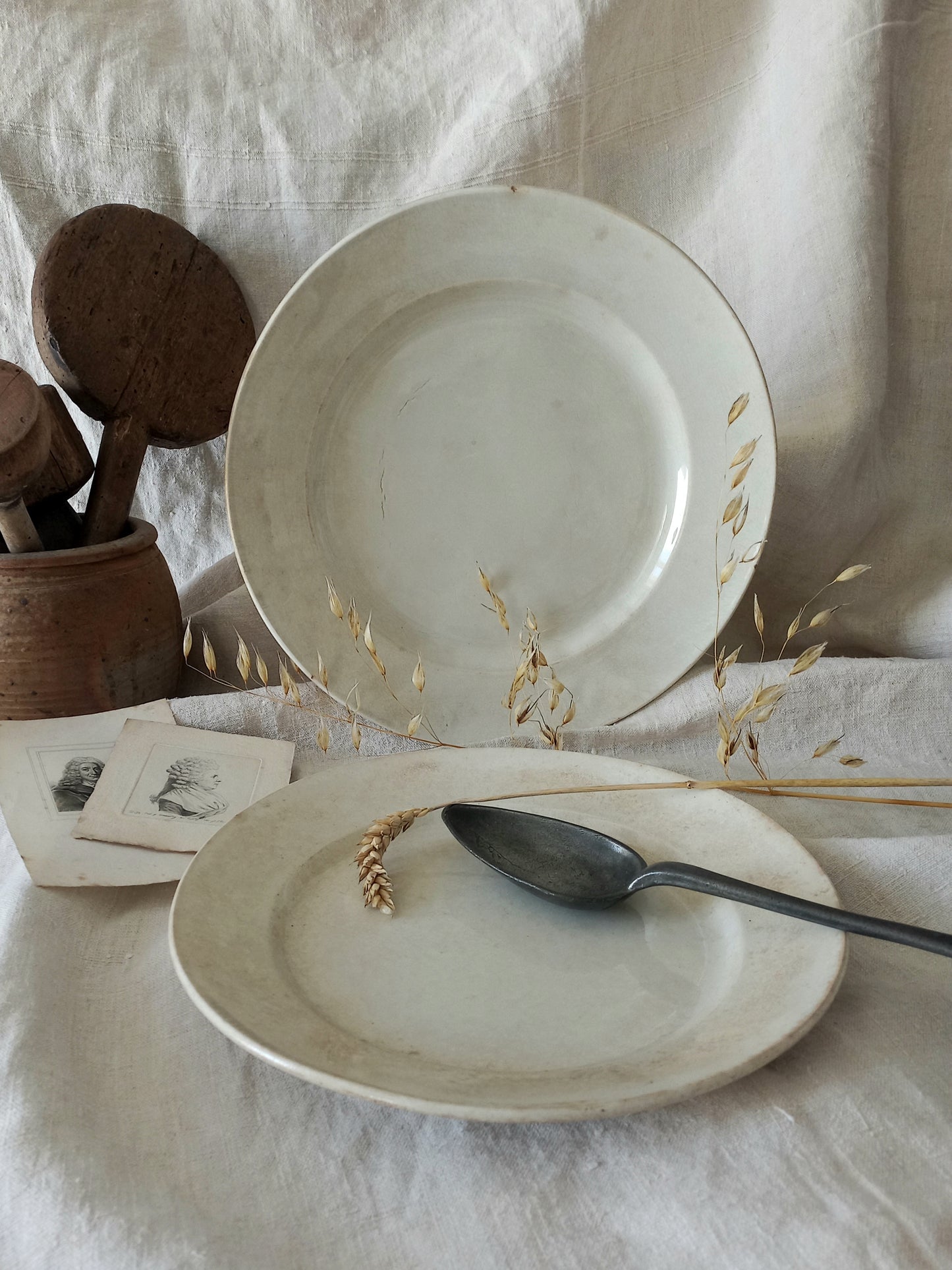 Two antique plates on a textured surface with a spoon and wooden items.