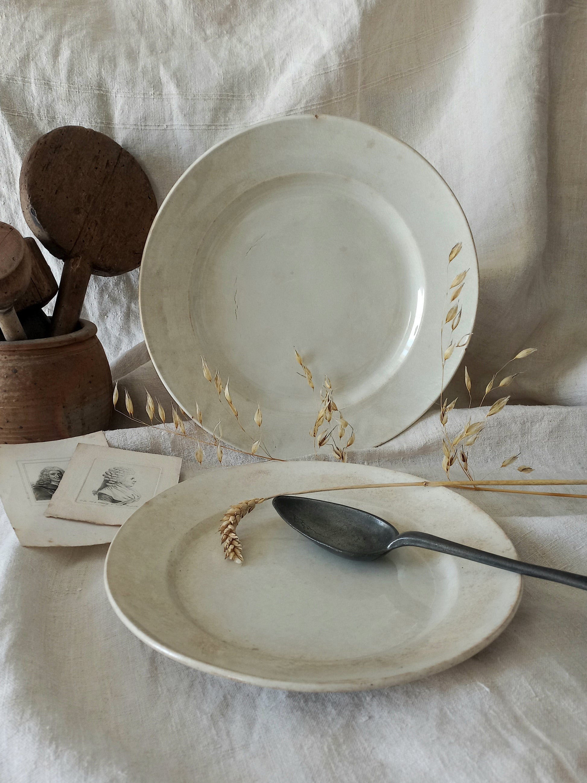 Two antique plates on a textured surface with a spoon and wooden items.