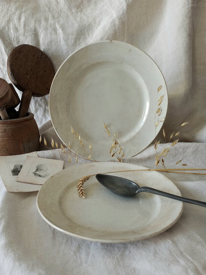 Two antique plates on a textured surface with a spoon and wooden items.