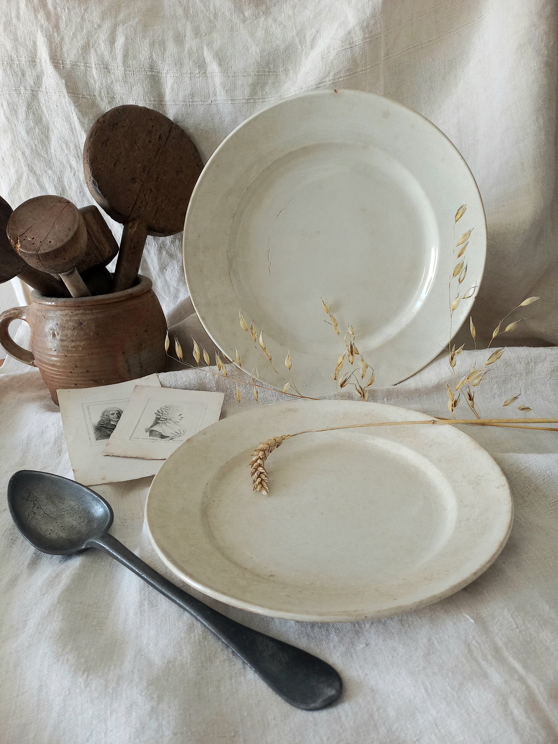 Set of antique plates on a textured surface with a spoon and wooden items.