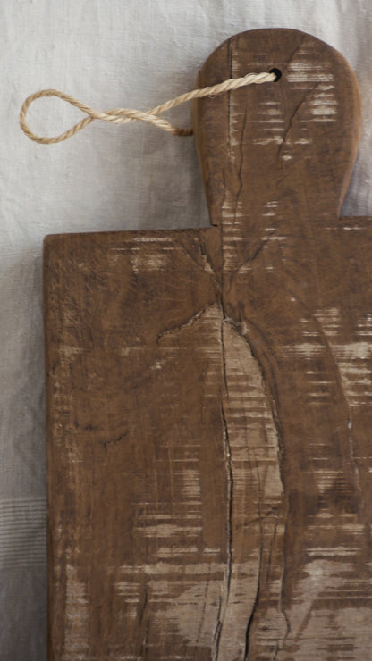 A large vintage wooden chopping board from south west France, shaped by years of use and hand-worn edges. Its rough texture and deep patina tell the story of daily bread, shared meals, and time well lived.