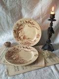 Two decorative antique plates with intricate floral and bird designs on a surface with a candle and paper.