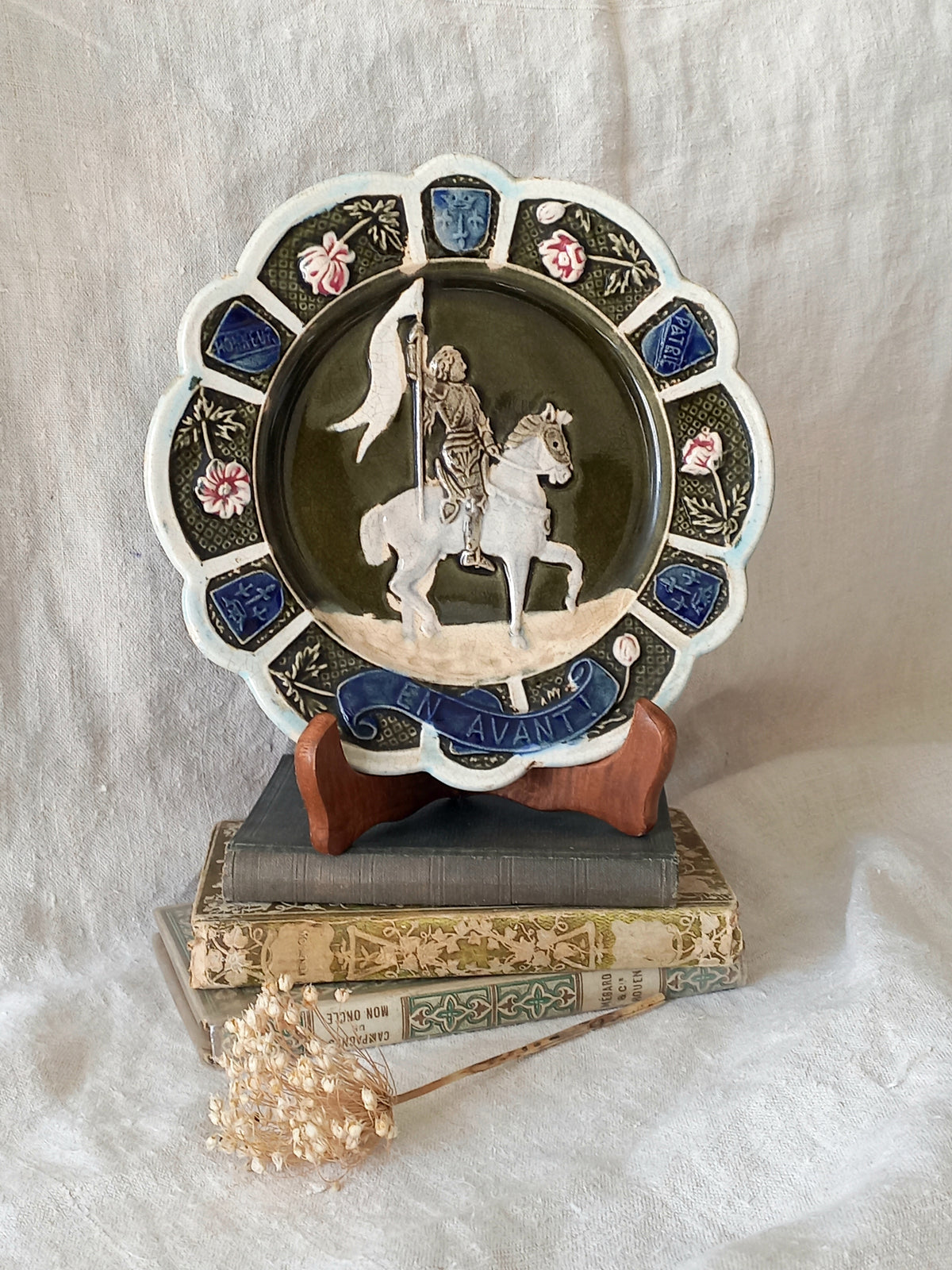 Decorative plate with a scene of Joan of Arc on a horse, surrounded by decorative elements on a white background.