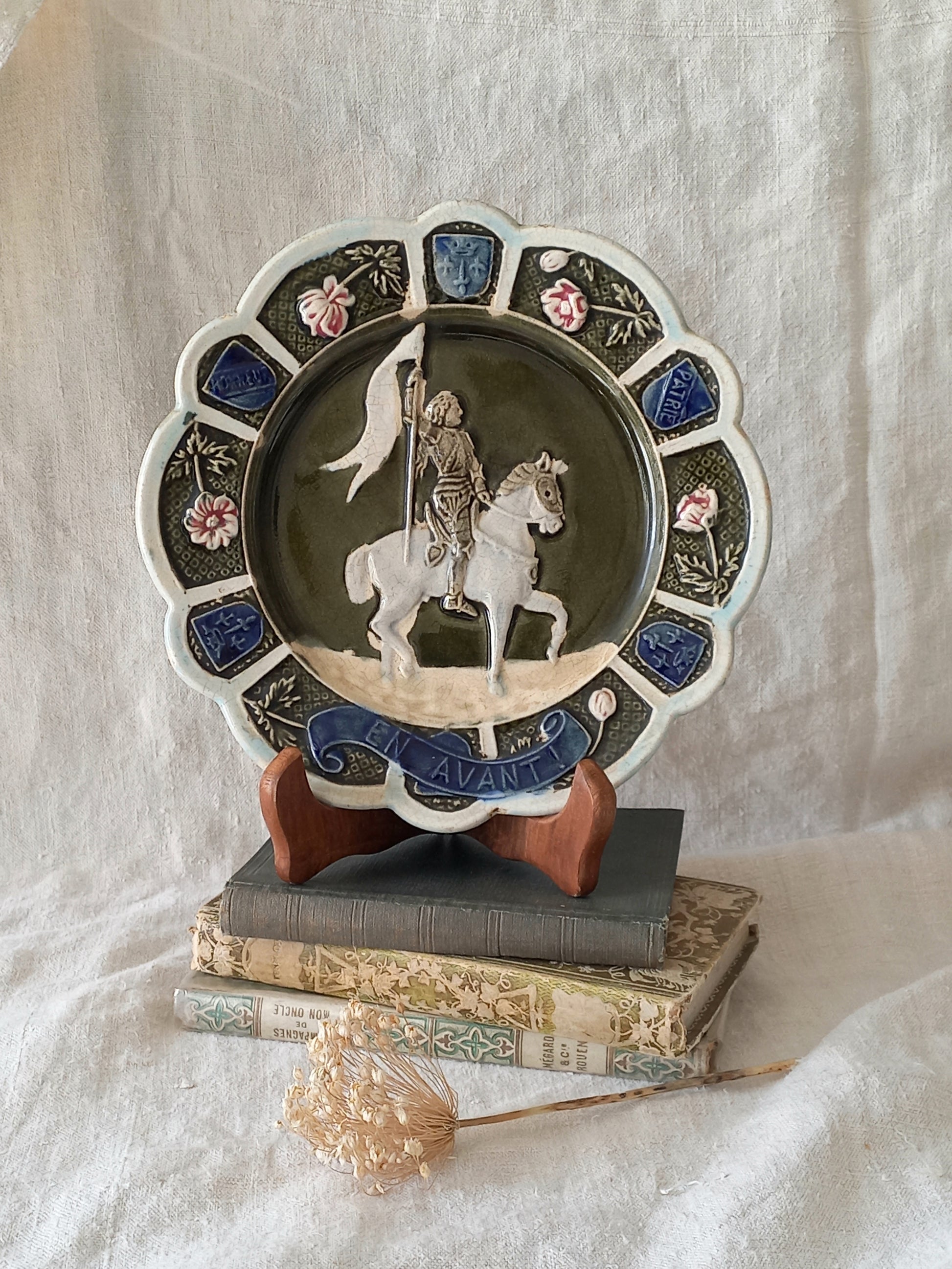 Decorative plate with a scene of Joan of Arc on a horse, surrounded by decorative elements on a white background.
