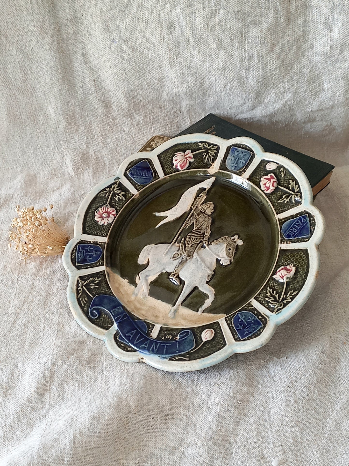 Decorative plate with a scene of Joan of Arc on a horse, surrounded by decorative elements on a white background.