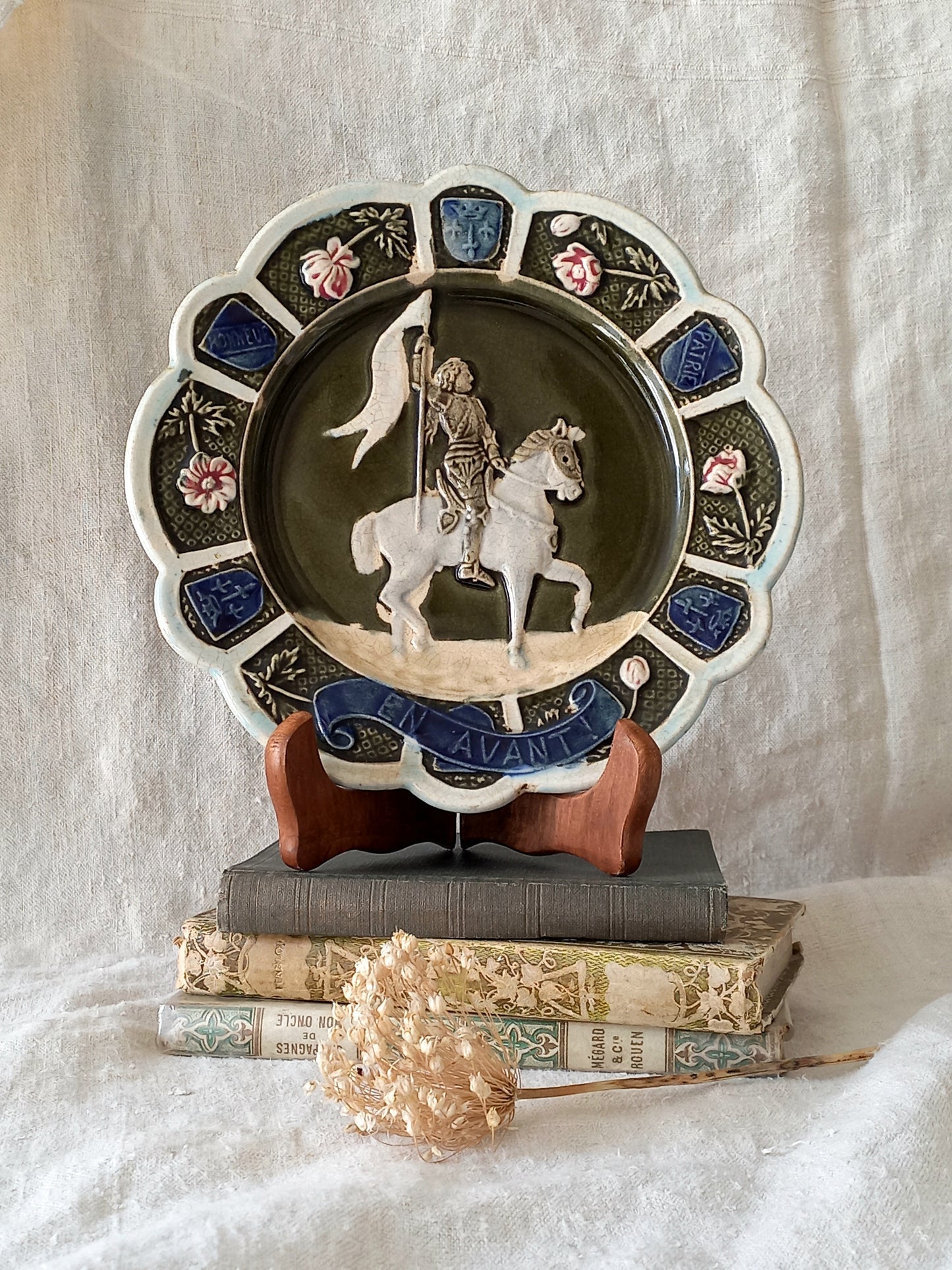 Decorative plate with a scene of Joan of Arc on a horse, surrounded by decorative elements on a white background.