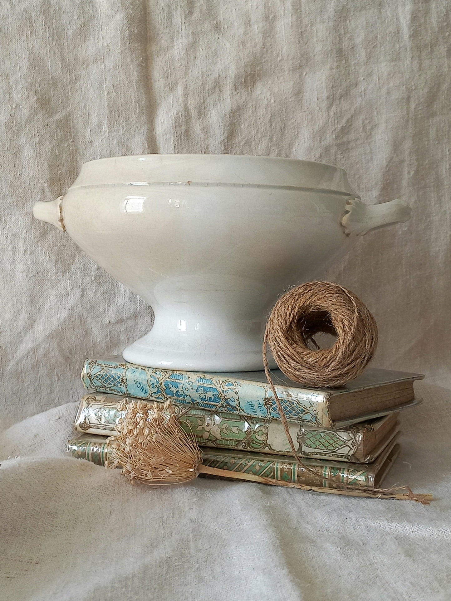White ironstone tureen bowl with a roll of twine and books on a textured fabric background