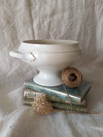 White ironstone bowl on a stack of books with twine and dried flowers against a textured fabric background