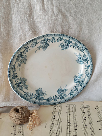 A round white ceramic plate with a blue floral border, styled on a beige linen cloth with a ball of twine, dried flowers, and sheet music underneath.