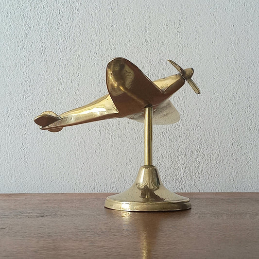 Brass airplane model on a stand against a plain background