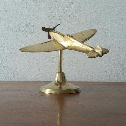 Brass airplane model on a stand against a plain background