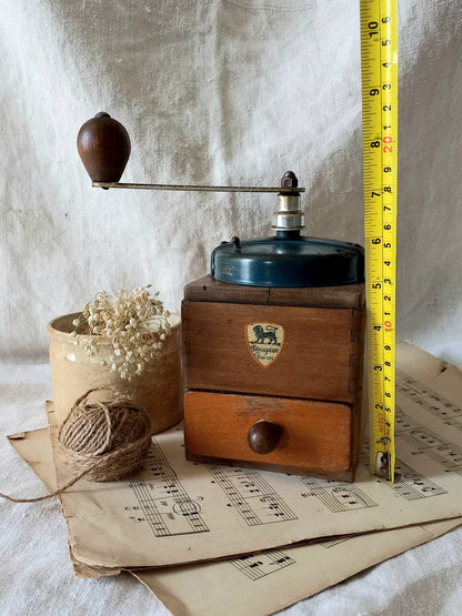 Vintage wooden coffee grinder with a measuring tape for scale on a textured surface.