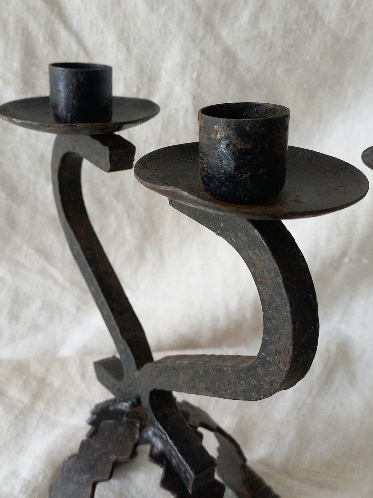 Wrought iron candle holder with two black candle cups on a textured white background