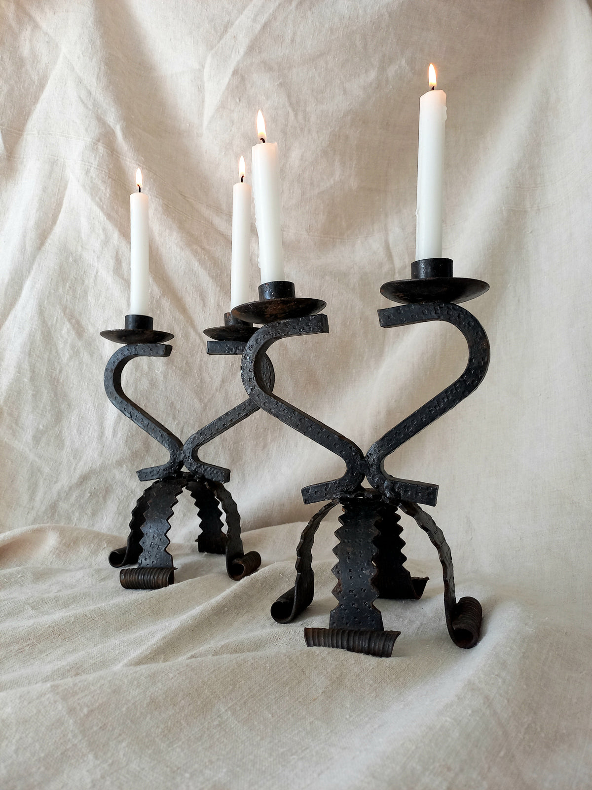 Wrought iron candle holders with candles on a textured white fabric background
