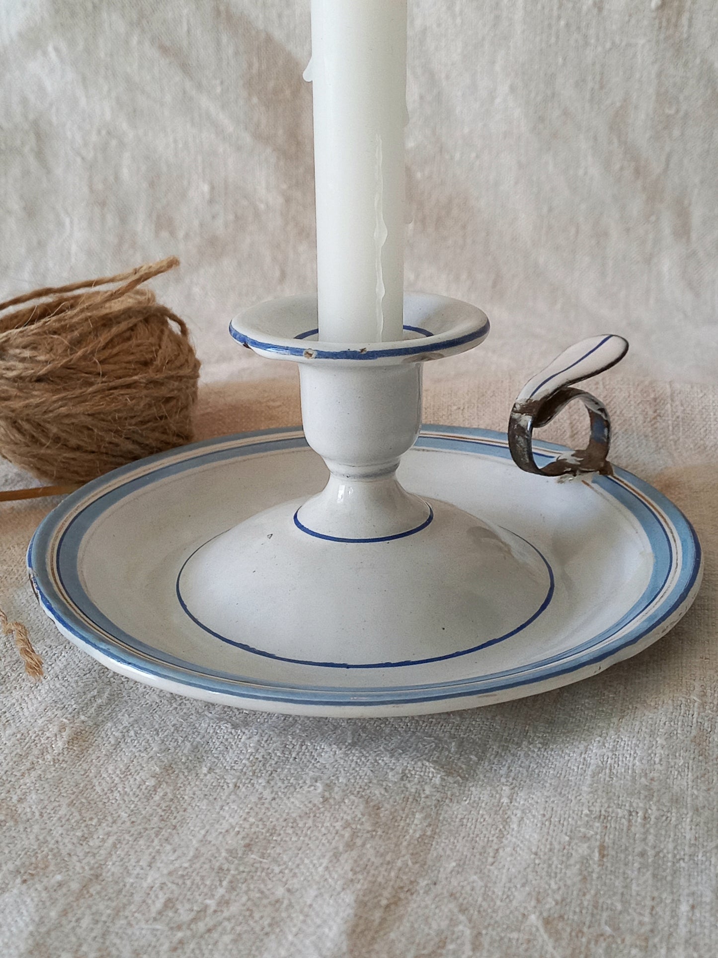 enamel candle holder with a white candle on a textured surface