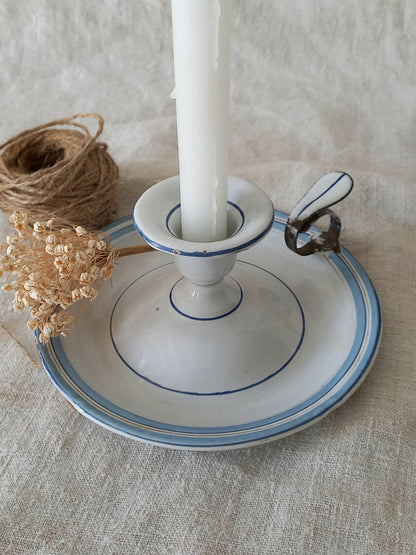 Candle in a white enamel holder with blue rim on a textured surface