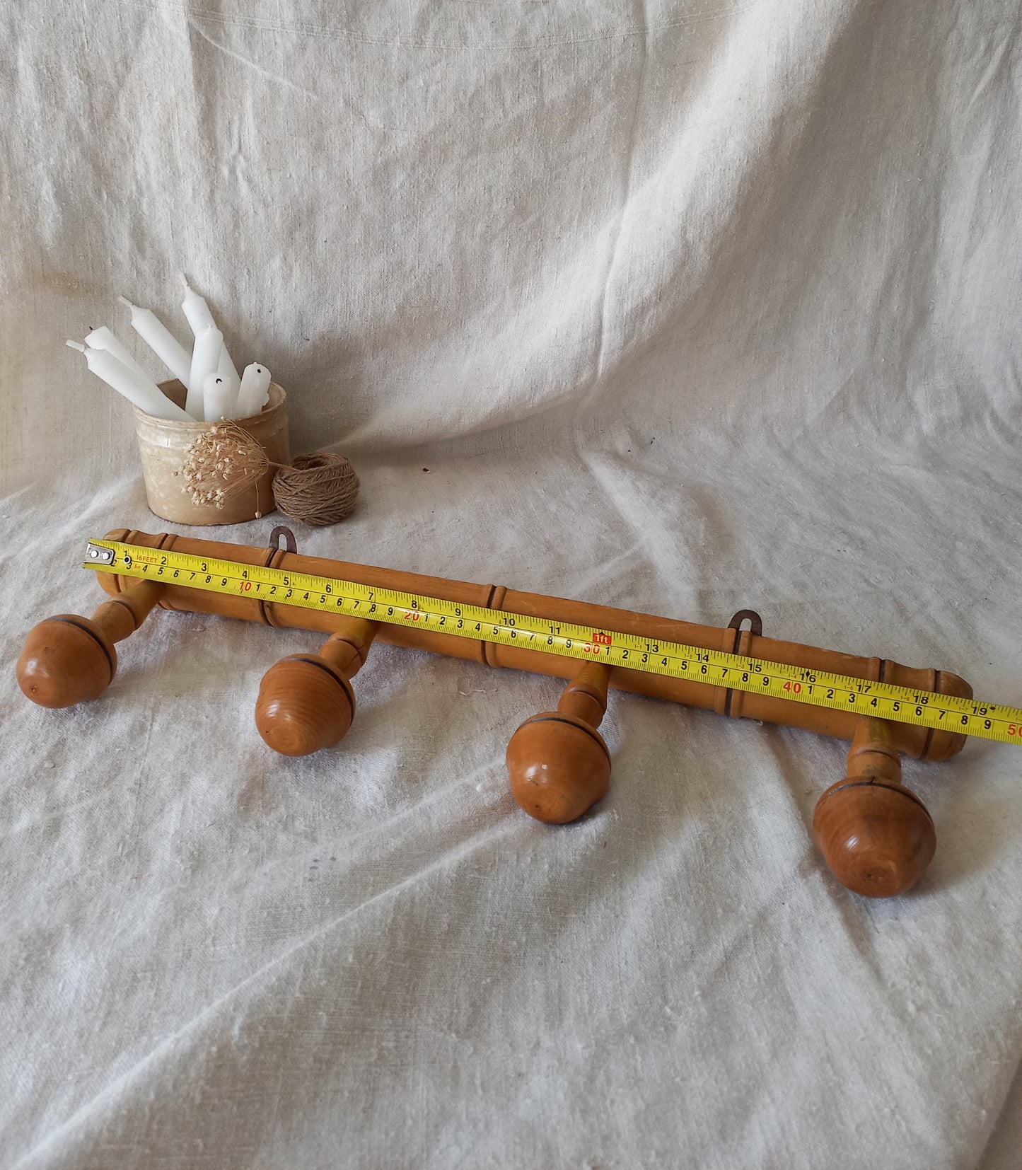 4 peg faux bamboo wooden coat rack on a textured white fabric background with a tape measure for reference