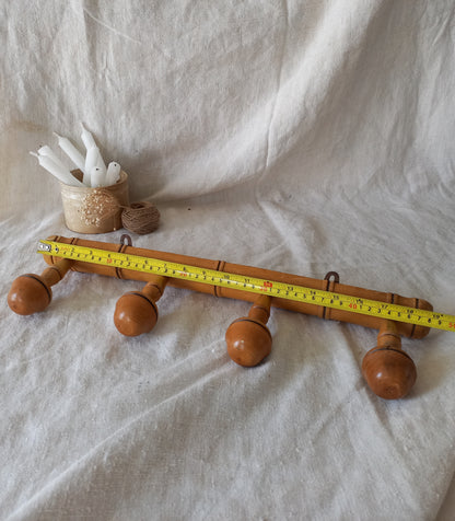4 peg faux bamboo wooden coat rack on a textured white fabric background with a tape measure for reference