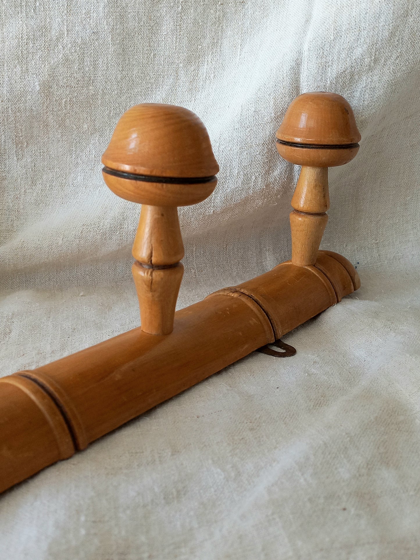 Close-up of a 4 peg faux bamboo wooden coat rack on a textured white fabric background