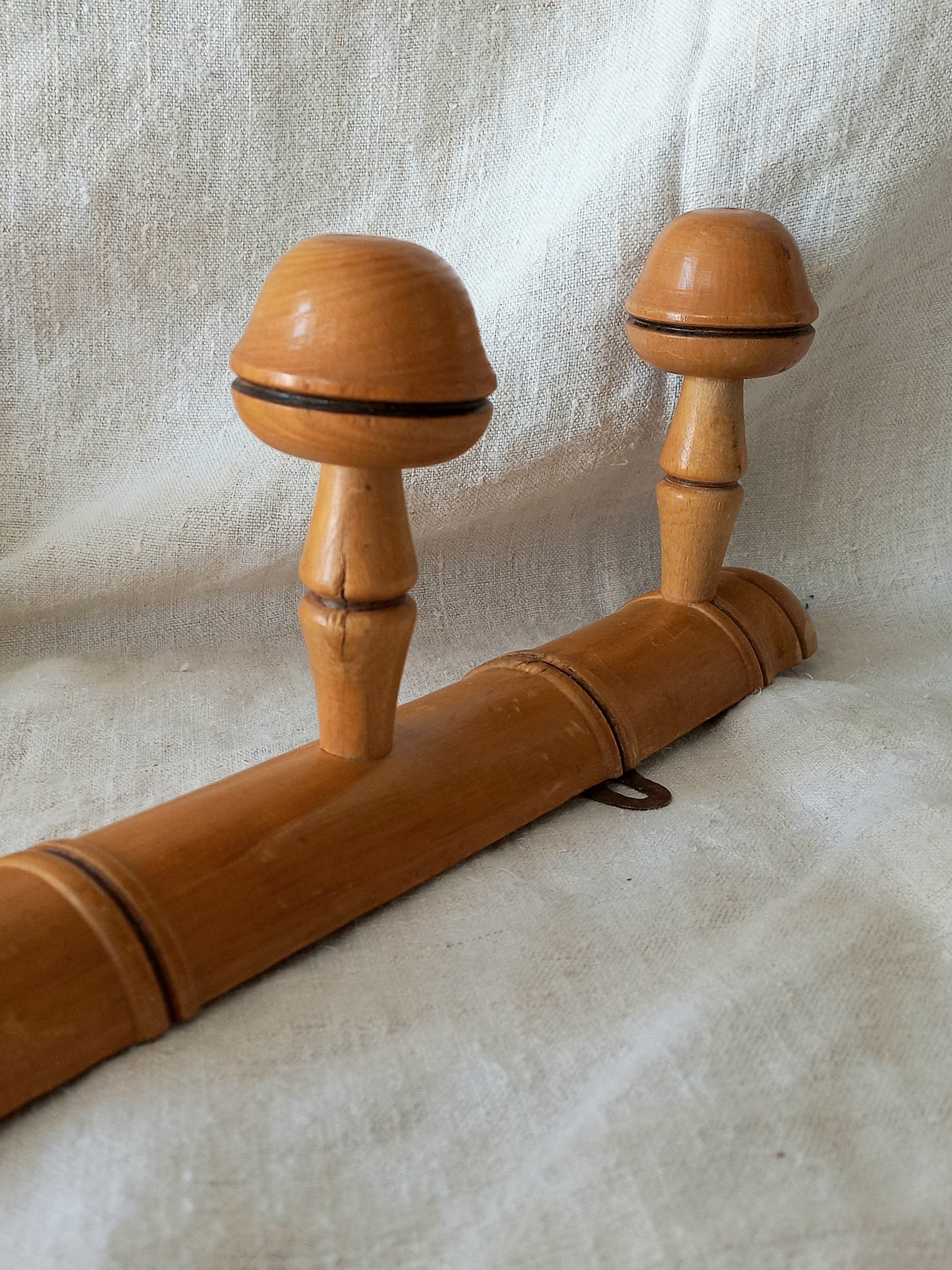 Close-up of a 4 peg faux bamboo wooden coat rack on a textured white fabric background