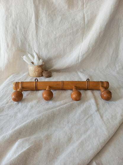 4 peg faux bamboo wooden coat rack on a textured white fabric background