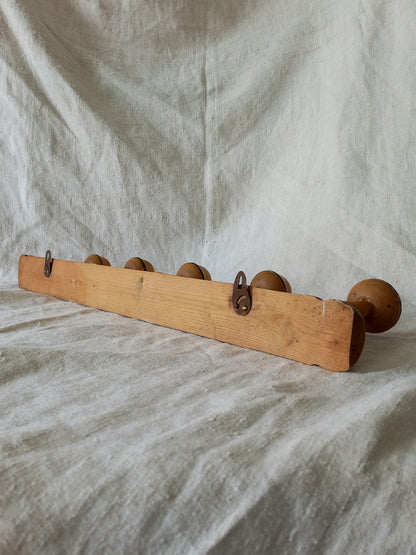 Rear of wooden coat rack with 5 hooks on a textured fabric background