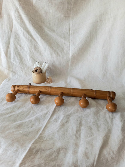 Wooden coat rack with five hooks on a textured white background