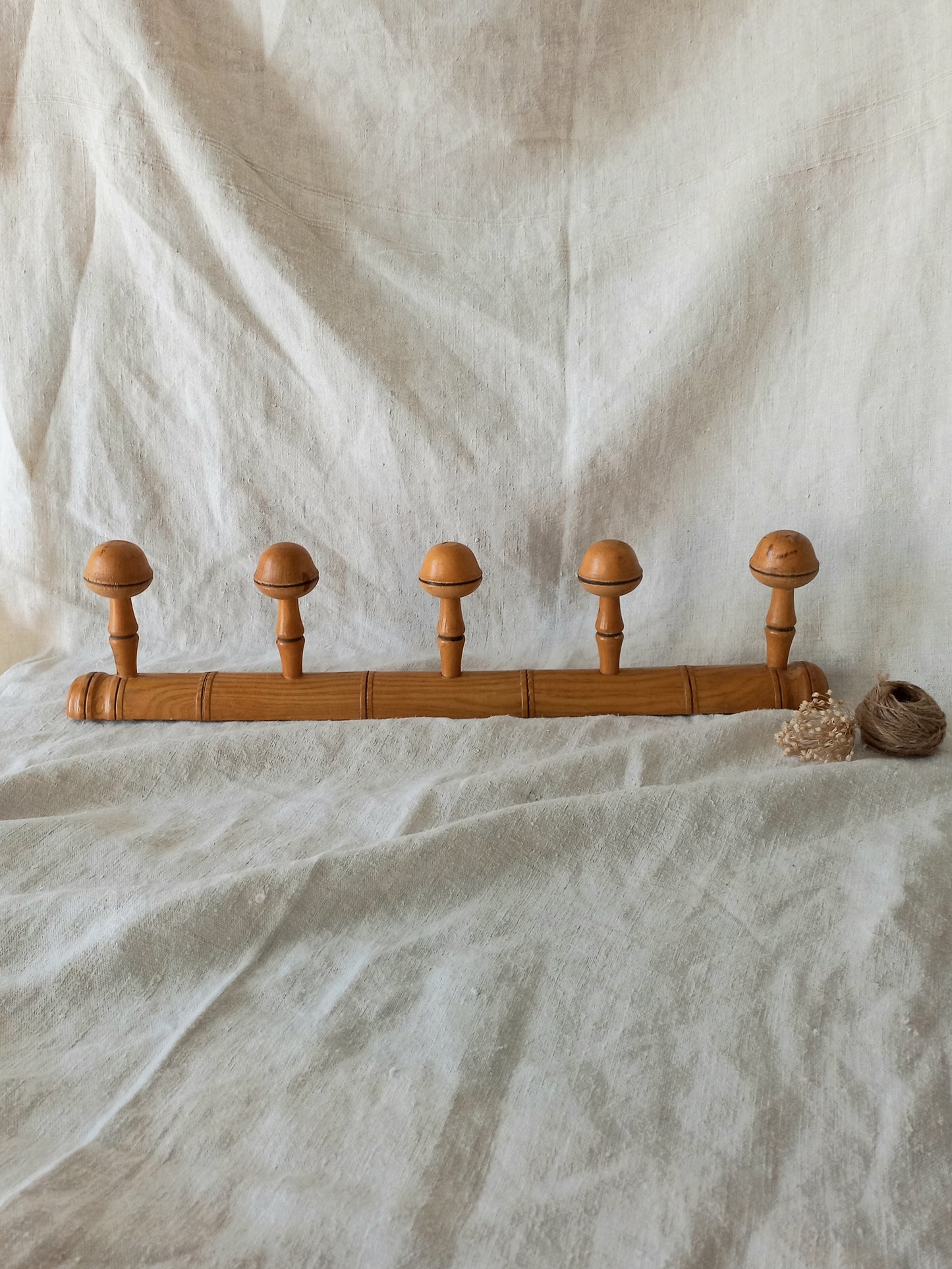 Wooden garment rack with five round wooden pegs on a textured white fabric background